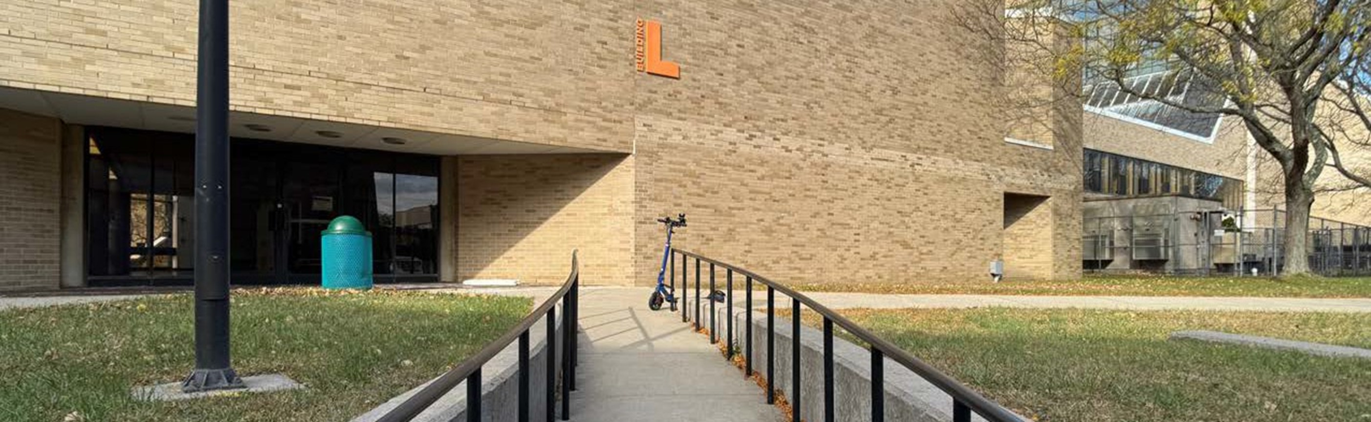 Library side entrance Photo of a ramp outside of one of the Library building entrances with a big, orange letter L on the bulding.