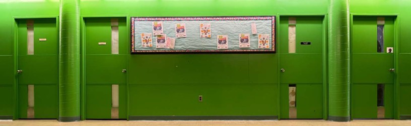 Green cluster classroom doors. Photo of the green cluster hallway with four doors and a bulleting board on the wall.