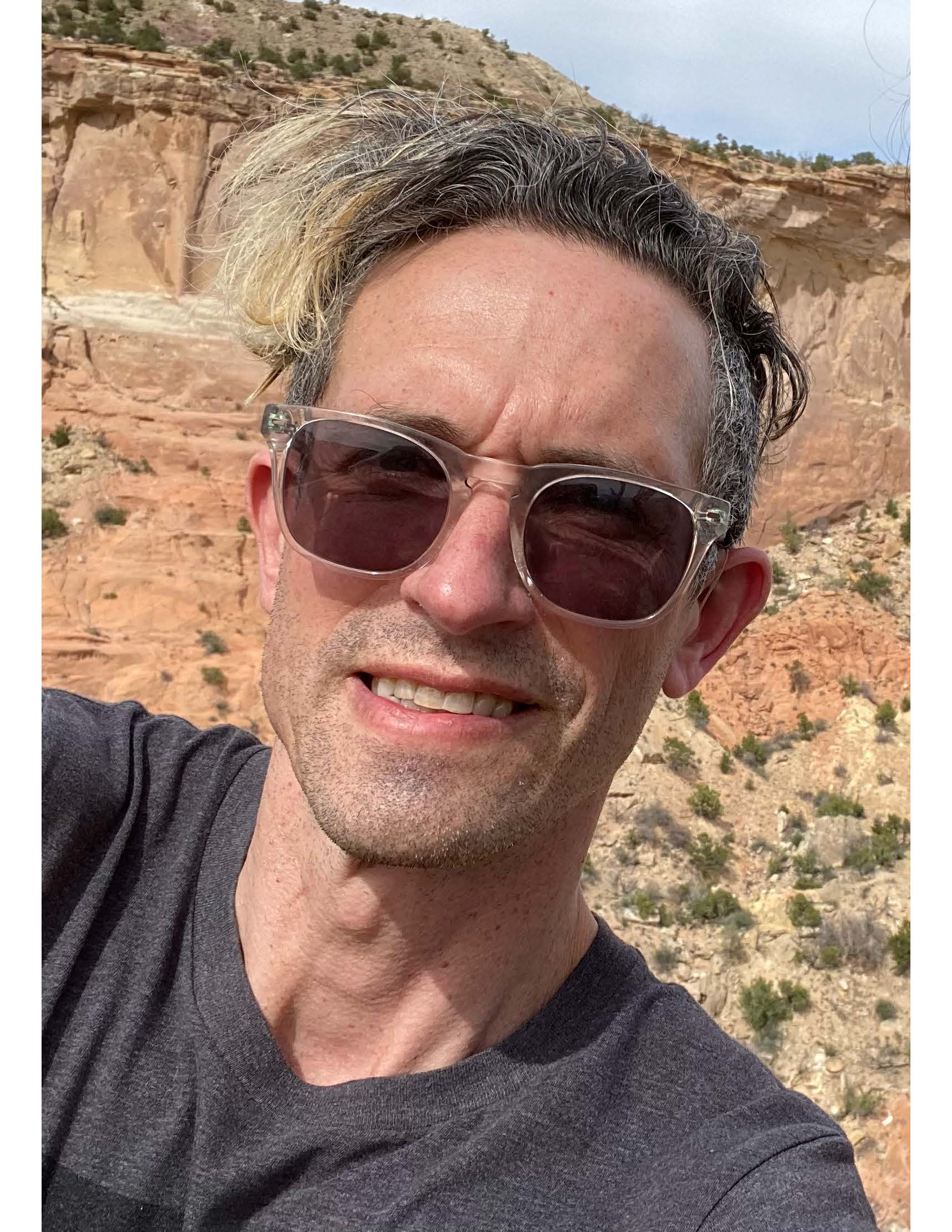 Man in sunglasses and grey t-shirt outside in a desert-type setting