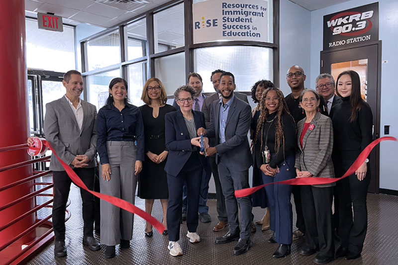 Elected officials, CUNY and PSC representatives join KCC President Suri Duitch and staff cut a red ribbon with large scissors in front of the new Resources for Immigrant Student Success in Education or RISE Center. 